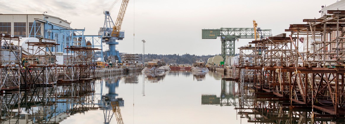 Two submarines scheduled for recycling are moved into Dry dock #2 at Puget Sound Naval Shipyard & Intermediate Maintenance Facility in Bremerton, Washington. Building 460 sits to the left (east) of the dry dock and the historical hammerhead crane is at the end of Pier 6 on the right (west) of Dry dock #2.